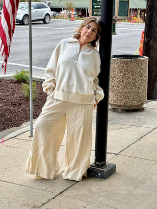 Woman in a cream-colored outfit standing on a sidewalk next to a streetlight.
