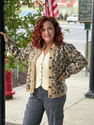 Woman wearing a leopard print cardigan on a city street with an American flag in the background.