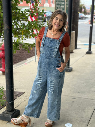Woman wearing distressed denim overalls with rust color shirt underneath