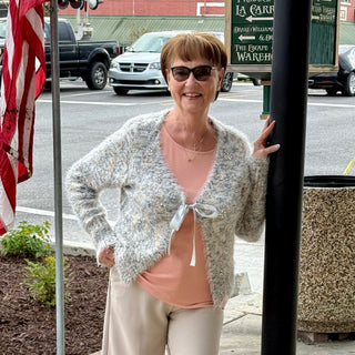 Woman standing on a street corner wearing sunglasses and a light gray cardigan.
