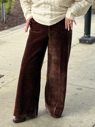 Person wearing a cream sweater and brown wide-leg pants on a sidewalk.