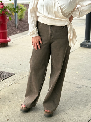 Person wearing a white blouse and brown wide-leg pants on a sidewalk.