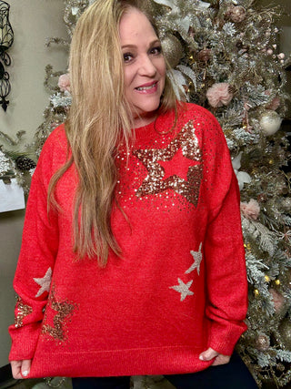 Woman wearing a red sweater with star patterns in front of a decorated Christmas tree.