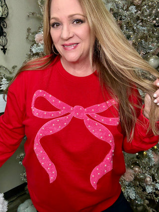 Woman wearing a red sweater with a pink bow design in front of a decorated Christmas tree.