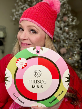 Person wearing a red knit hat holding a colorful product packaging with 'musee MINIS' branding.