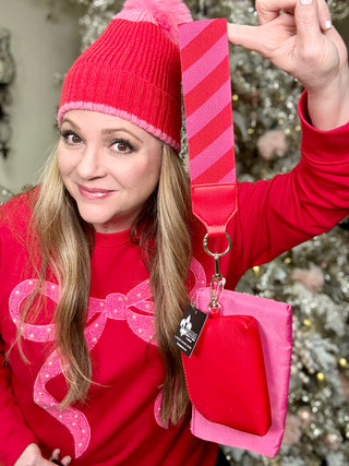 Person wearing a red outfit with a matching pink bag and accessories, standing against a blurred festive background.