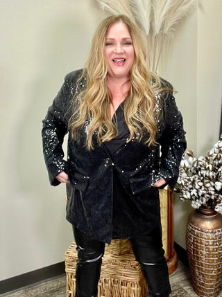 Woman standing with sequin blazer with faux leather leggings.