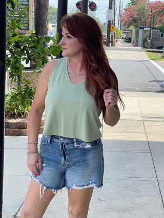 Woman standing on sidewalk wearing green tank top with blue denim jean shorts