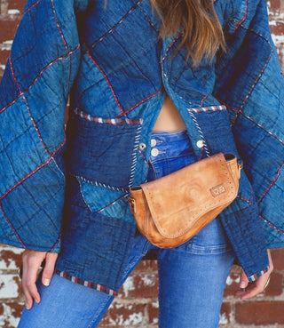A person wearing a blue denim jacket with a checkered pattern and a brown purse with a zipper.