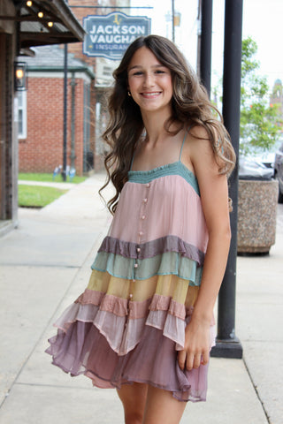 A girl wearing a multicolored tiered layered dress with a V-neckline and buttons down the front, standing outdoors.
