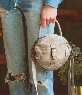 A person wearing blue denim jeans holding a beige, faux leather BedStu Arefield Icicle DD handbag.