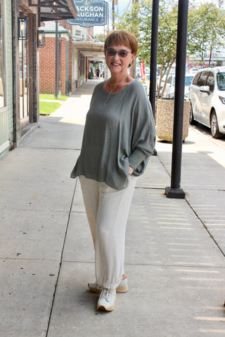 Lady standing on sidewalk wearing grey long sleeve shirt paired beige linen pants.