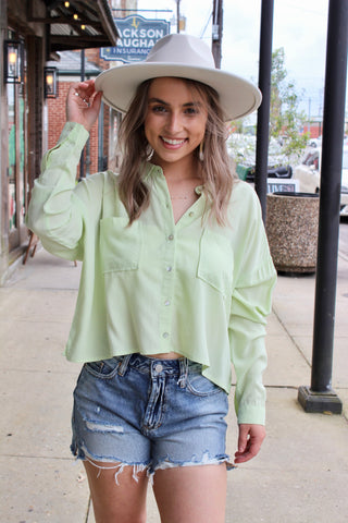Woman wearing a green long sleeve shirt paired with blue denim Jean shorts and a cream hat