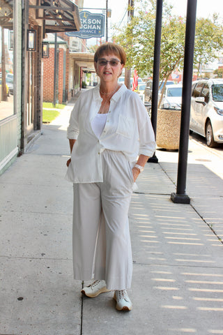Lady standing on sidewalk wearing a cream long sleeve button up with ecru wide leg pants with tennis shoes.