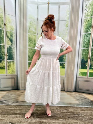 Woman wearing a white dress standing in a room with large windows.