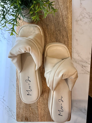 Pair of beige sandals with 'Miu Miu' branding on a wooden board with a marble background.