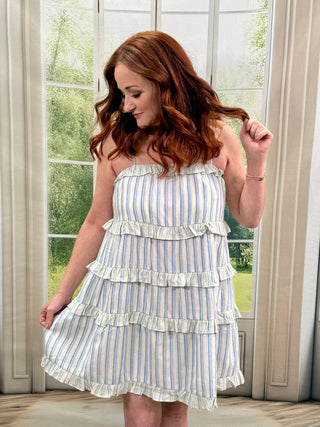 Woman with White & Blue stripe dress standing in front a window.