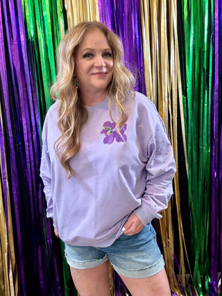 Woman wearing a light purple sweatshirt with a graphic design in front of colorful streamers.