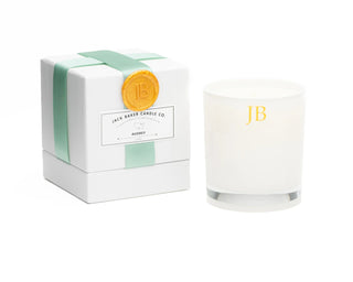 White candle with 'JB' branding next to its packaging on a white background