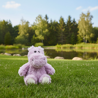 Purple hippo plush toy on grass with a pond and trees in the background