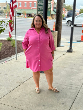 Woman in a pink dress standing on a sidewalk with a street and buildings in the background