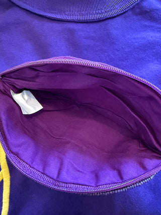 Close-up of a purple zippered pocket on a matching purple garment, showing the interior lining and a small white tag.