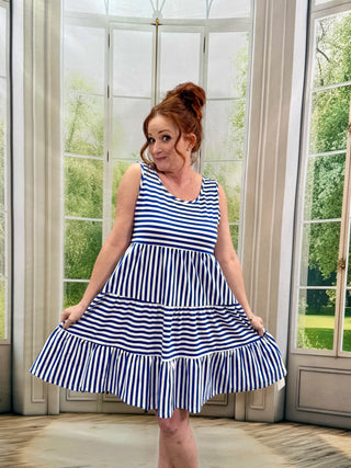 Woman wearing a blue and white striped dress standing in a room with large windows.