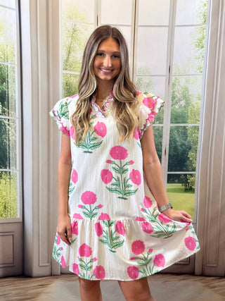 Woman wearing a floral dress standing in a room with large windows.