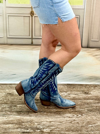 Blue cowboy boots worn with denim shorts on a wooden floor.
