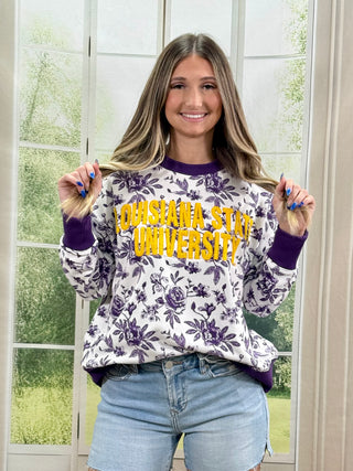 Person wearing a floral sweatshirt with 'Louisiana State University' text, standing in front of a window.