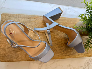 Pair of blue high-heeled sandals on a wooden surface with a plant in the background.