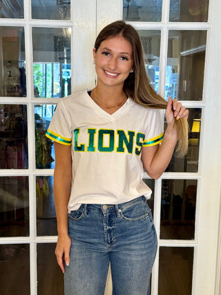 White V-neck shirt￼ With the writing “Lions” on the front with the color, green and outlined in yellow￼. Green and yellow sequin stripes on the sleeve￼