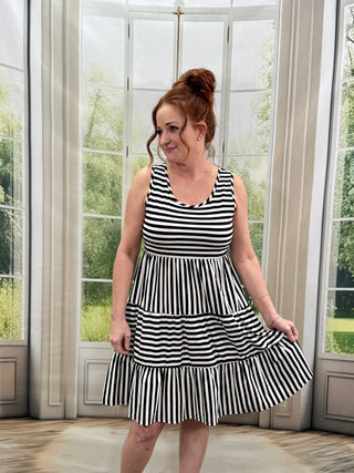 Woman wearing a black and white striped dress standing in a room with large windows.