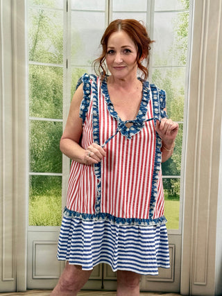 Woman wearing a red, white, and blue striped dress with ruffled details in front of a window.