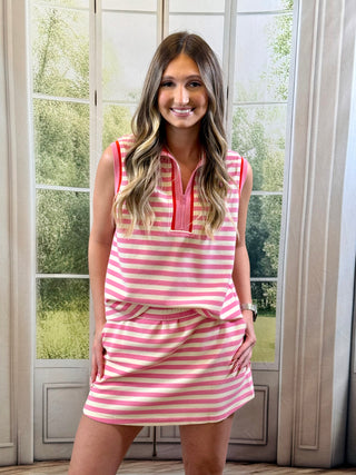 Woman wearing a pink and white striped dress standing in front of a large window with greenery outside.