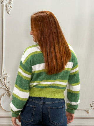 A woman with long red hair is shown from the back wearing a fuzzy knit sweater with horizontal stripes in green, lime green, and white, paired with blue jeans.