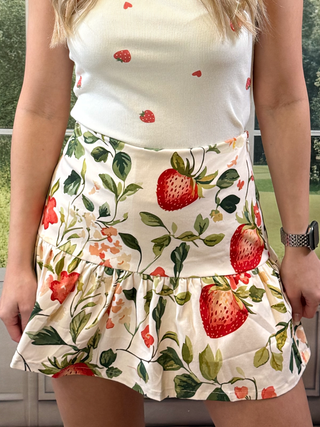Person wearing a white top and strawberry-patterned skirt outdoors.