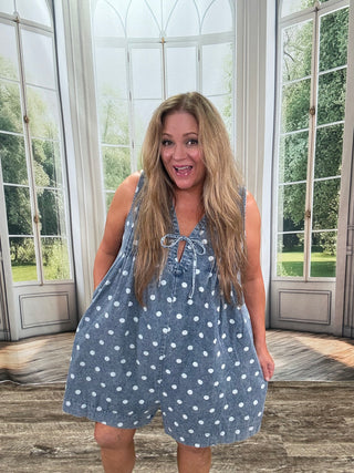 Woman wearing a blue polka dot dress standing in a room with large windows.