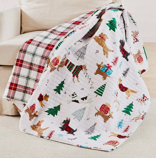 Two Christmas-themed quilts on a couch, one with plaid pattern and the other with dogs and trees.