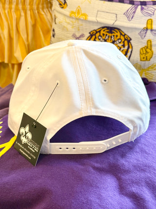 A white snapback cap shown from the back, resting on a purple fabric surface with a black hangtag attached.