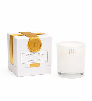 White candle with gold 'JB' logo next to its packaging box on a white background