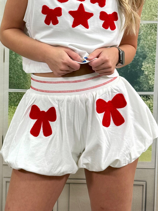 Person wearing a white outfit with red bows in front of a window.