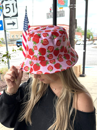 Person wearing a pink bucket hat with red strawberry pattern outdoors.