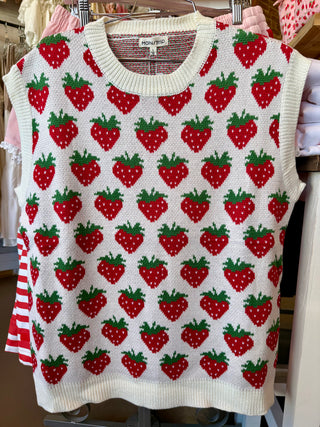 White sweater vest with red strawberry pattern on a hanger.