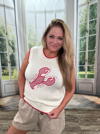Woman wearing a white sleeveless top with a red lobster design in a bright room with large windows.