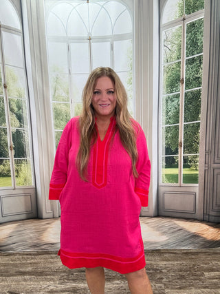 Woman wearing a bright pink dress with red accents in a room with large windows.