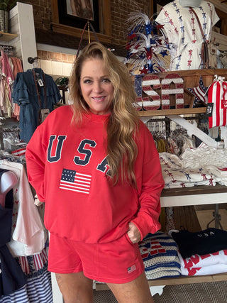 Woman wearing a red 'USA' sweatshirt with an American flag in a store setting.