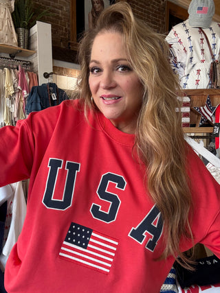 Woman wearing a red 'USA' sweatshirt with an American flag in a store setting.
