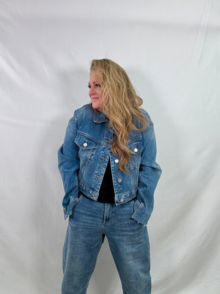 Person wearing a blue denim jacket and jeans against a white background