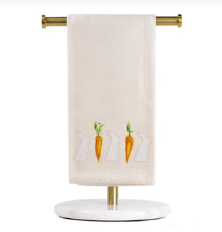 Beige towel with embroidered carrots and bunnies hanging on a gold towel rack.